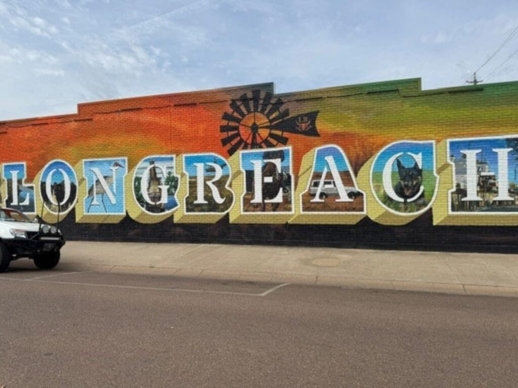 Colourful Longreach mural on a brick wall, featuring large lettering, a windmill and silhouettes of local landmarks.