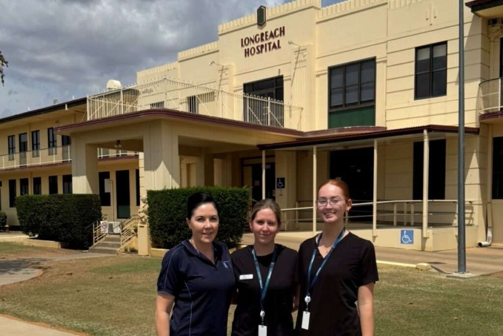 Three women, one wearing an LTT polo shirt and two in black uniforms, stand outside Longreach Hospital.